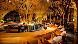 A bar area with a curved wooden counter, seating, and a bamboo ceiling structure. - Naman Retreat (Da Nang)