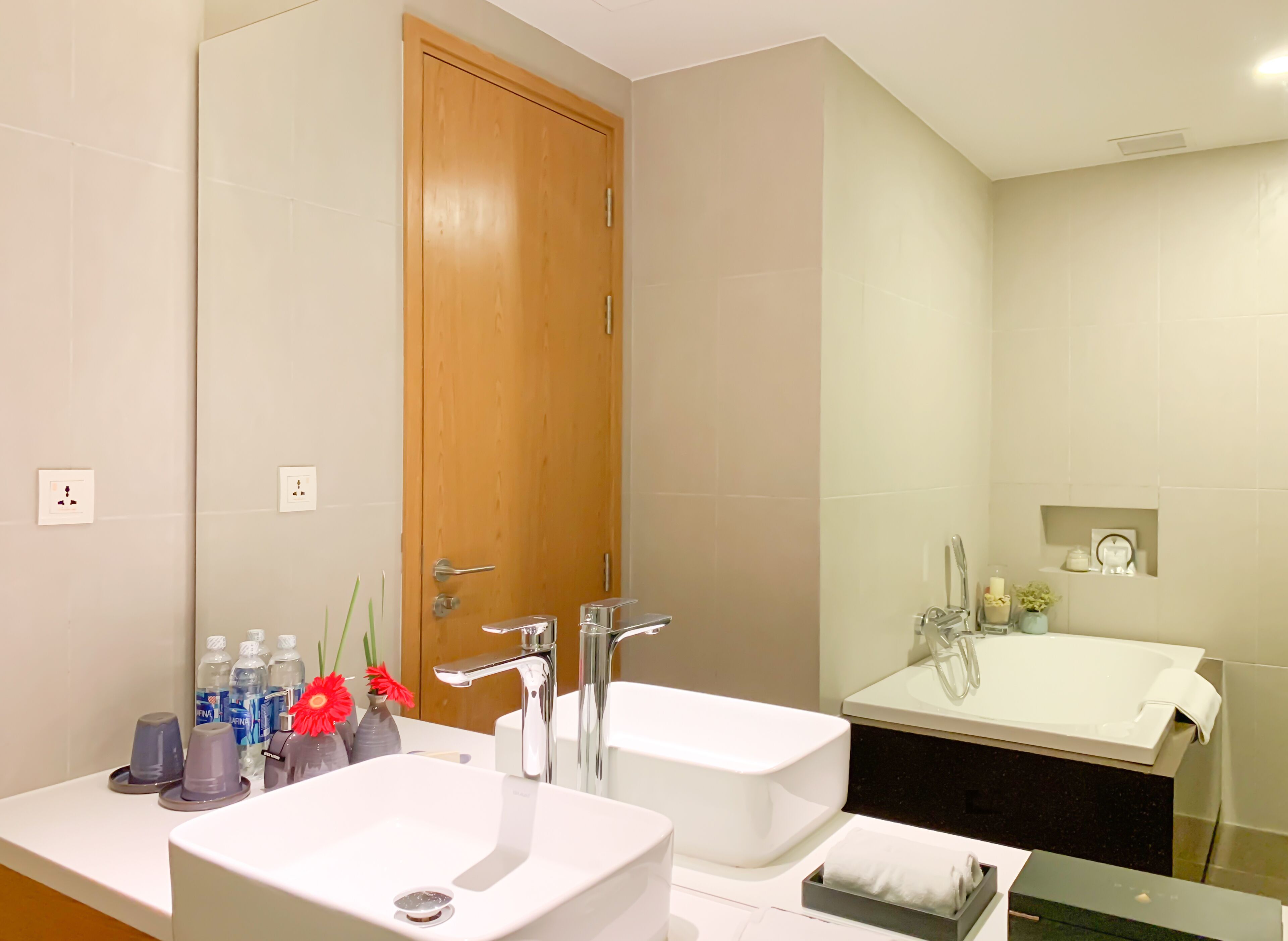 A modern bathroom with a wooden door, two sinks, a large mirror, and a bathtub.