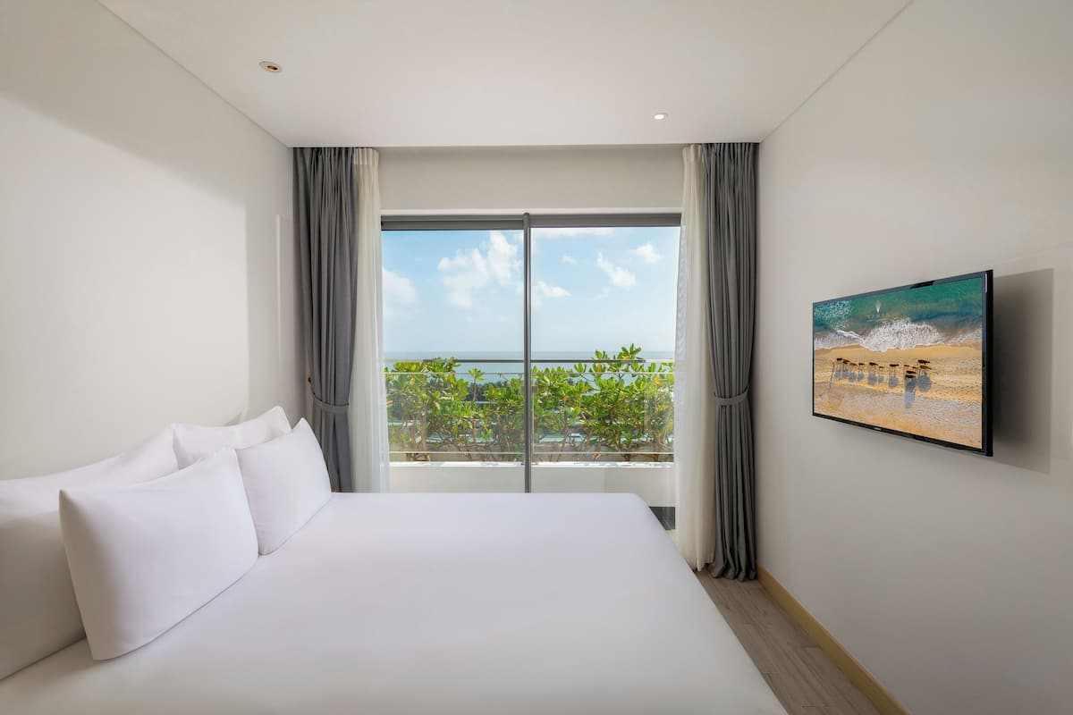 Une chambre d’hôtel avec un grand lit, une vue sur l’océan et un tableau représentant une scène de plage.