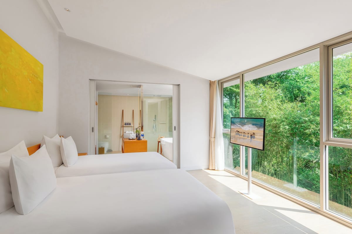 Une chambre d’hôtel moderne dotée d’un grand lit, d’une télévision et offrant une vue sur la verdure grâce à de grandes fenêtres.