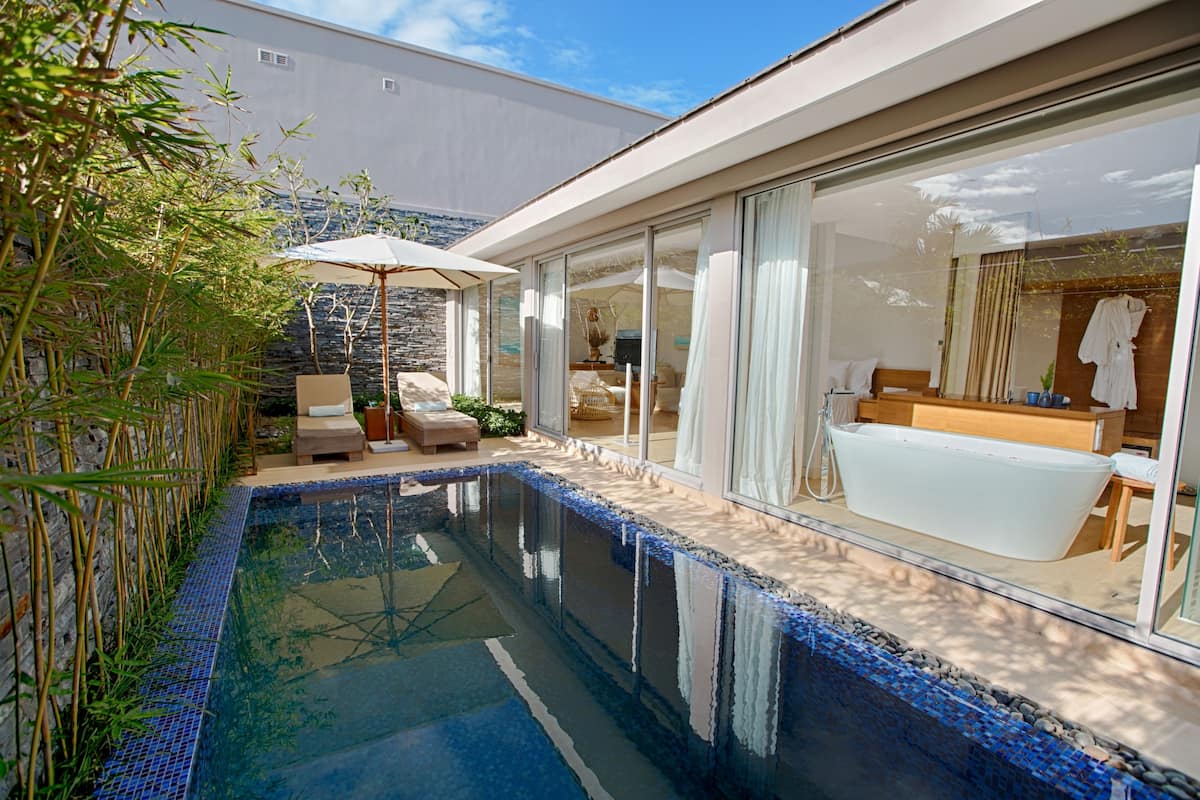 Un espace piscine moderne avec une piscine à l’eau cristalline, une terrasse en bois et une salle de spa entièrement vitrée.