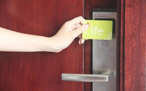 A hand holding a yellow card with the word "life" on it, inserting it into a door lock. - The Life Hotels (Surabaya)