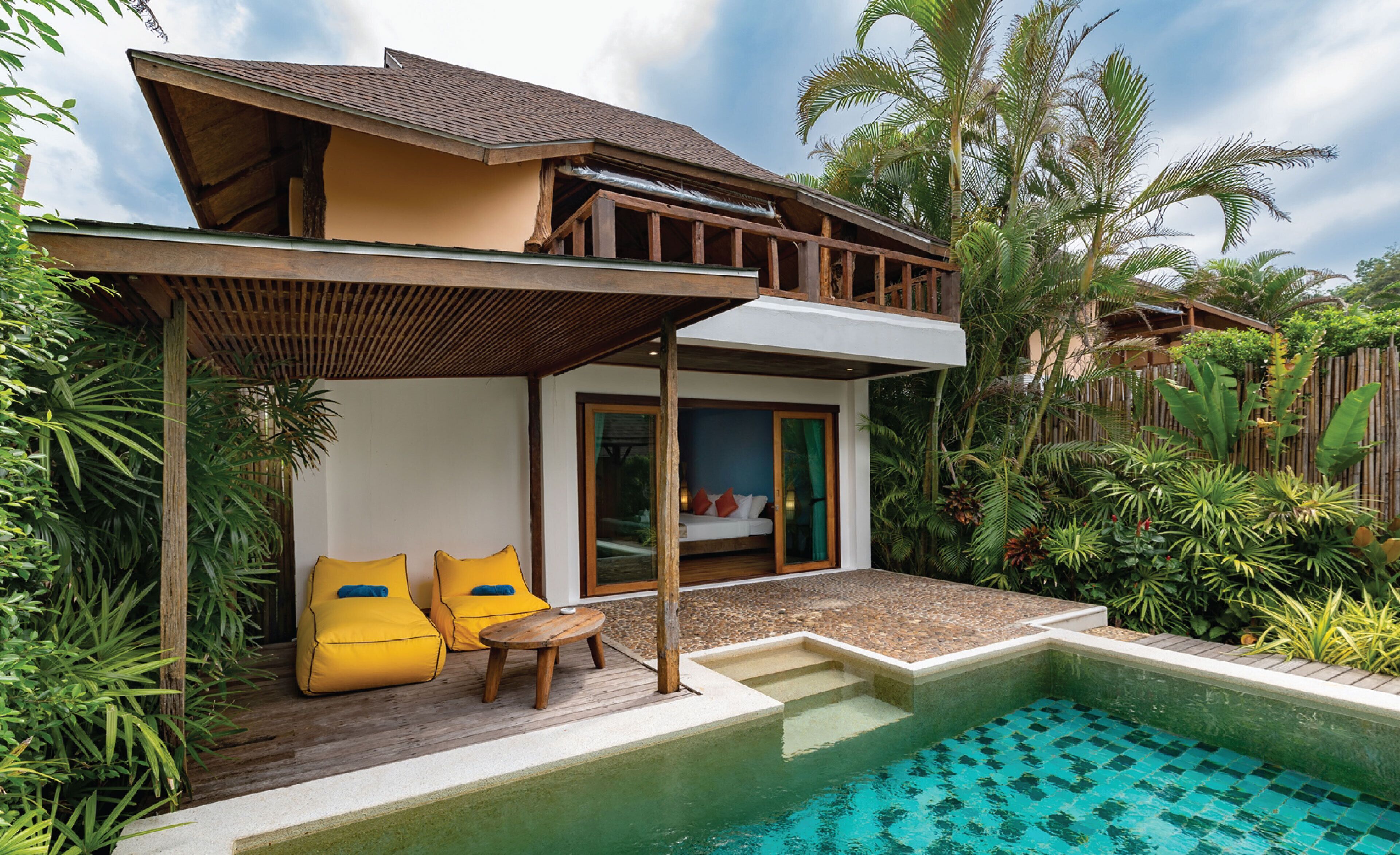 A two-story house with a pool, wooden deck, and tropical plants.