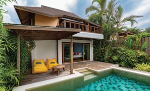 A two-story house with a pool, wooden deck, and tropical plants.