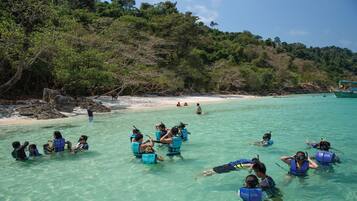 Un grupo de personas haciendo snorkel en aguas turquesas cristalinas, con un barco al fondo.