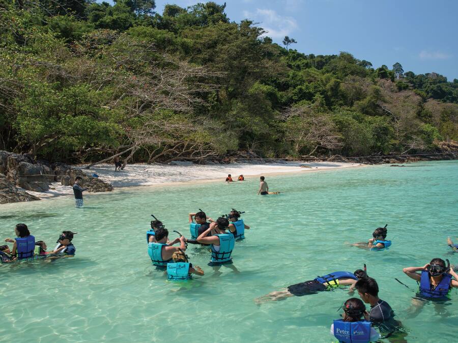 Un grupo de personas haciendo snorkel en aguas turquesas cristalinas, con un barco al fondo.