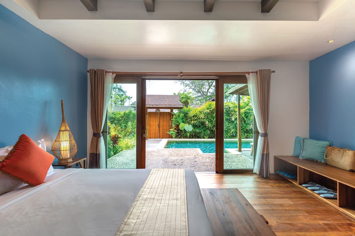 Quarto com cama grande, um banco de madeira e vista para piscina e jardim.