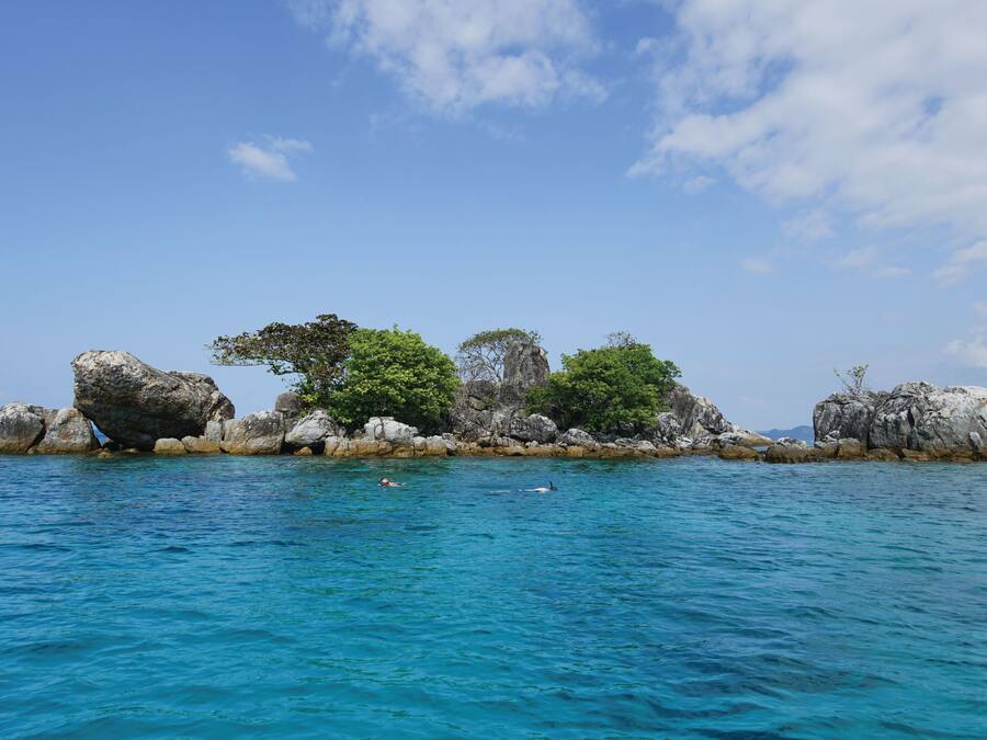 A rocky island with clear blue water and a few trees.