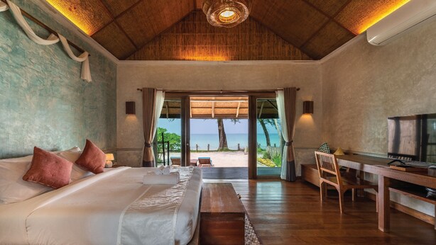 A bedroom with a bed, a desk, and a view of the beach. - Tinkerbell Resort (Ko Kood)