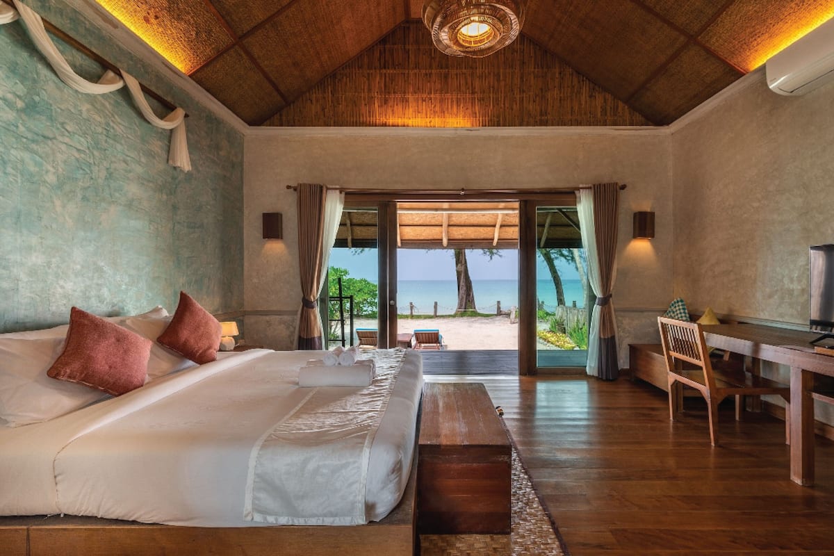 Um quarto com cama, escrivaninha e vista para a praia.