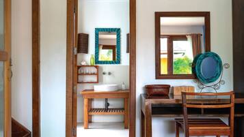 Una habitación con piso de madera, una mesa de madera con un sombrero, un espejo y una ventana con cortinas.