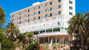 A multi-story hotel with balconies, a stone facade, and a palm tree in the foreground. - Globales Cala'n Blanes (Ciutadella de Menorca)