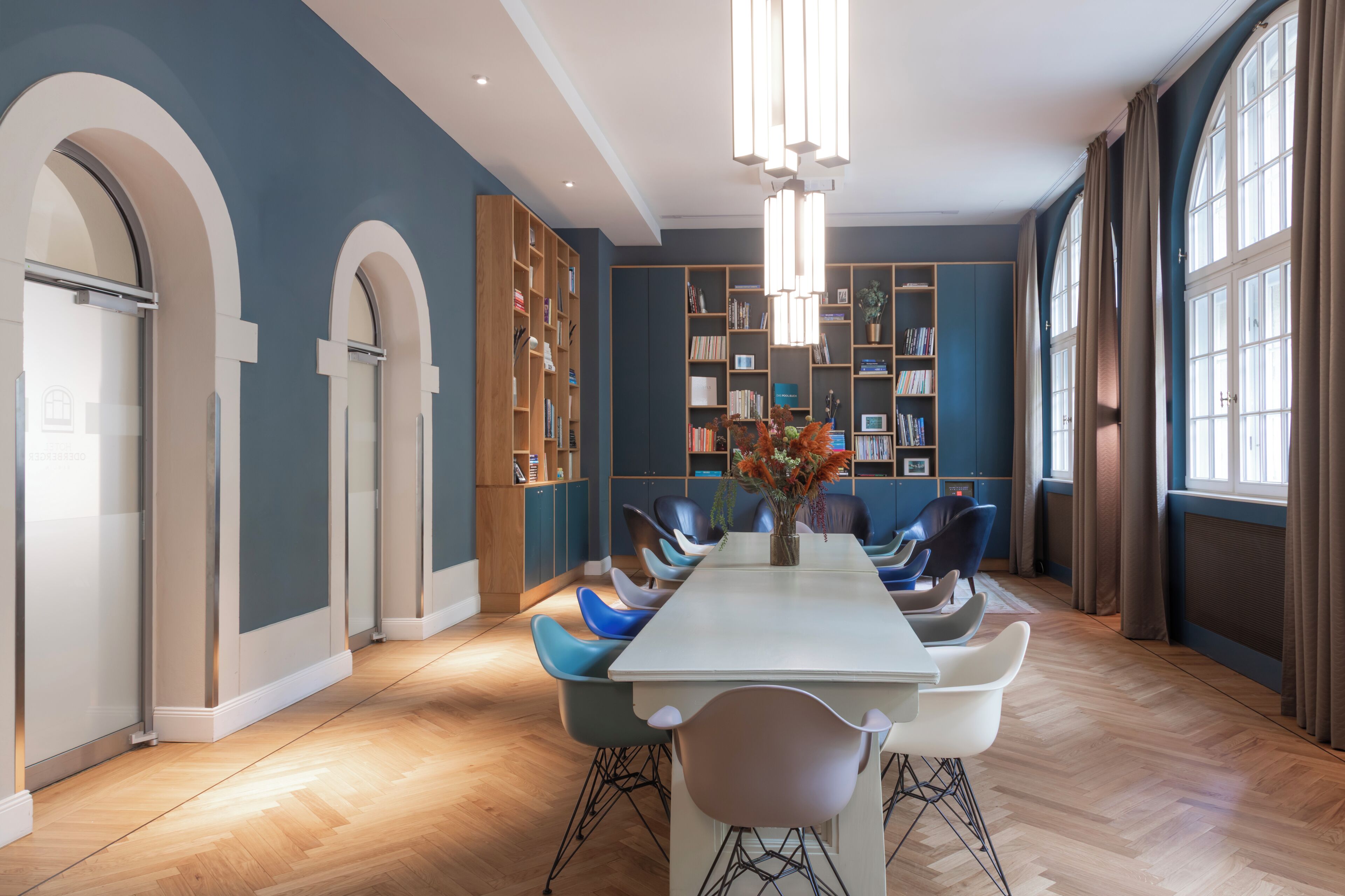 A modern dining room with a long table, blue chairs, and a central vase of flowers.