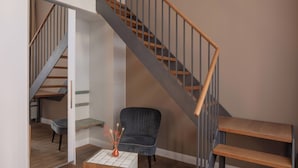 Una escalera con peldaños de madera y barandillas de metal, un sillón tapizado oscuro y una mesita con un jarrón.
