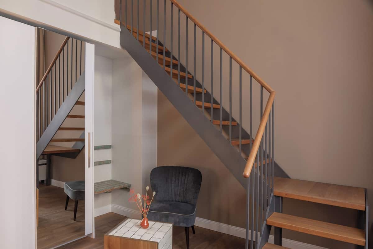 A staircase with wooden steps and metal railings, a dark upholstered chair, and a small table with a vase.