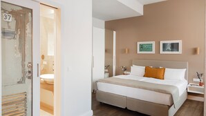 Un dormitorio moderno con una cama grande, una mesita de noche y un baño visible a través de una puerta abierta.