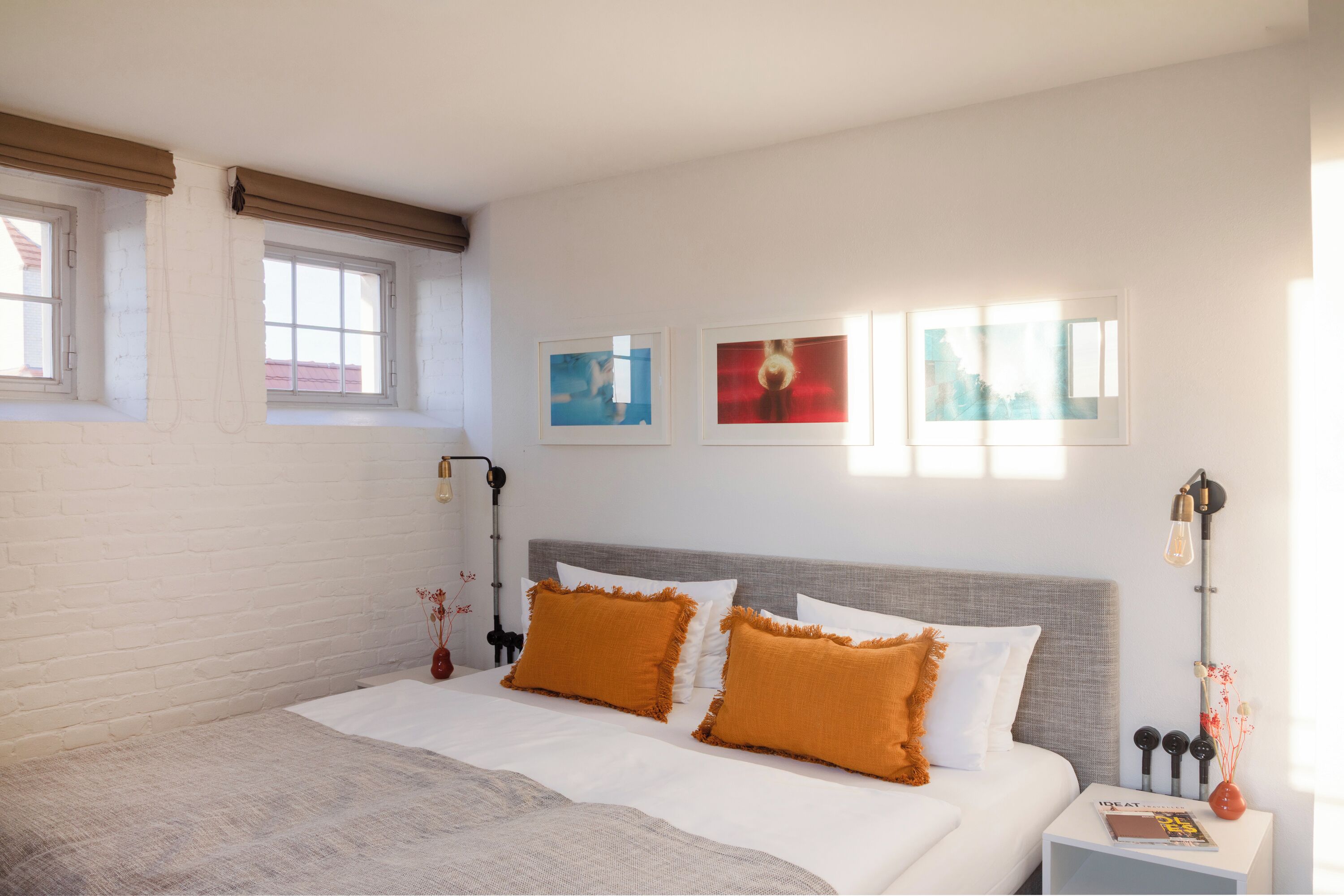 Ein Schlafzimmer mit einem Bett, zwei Kissen, einem Nachttisch, einer Lampe und drei gerahmten Bildern an der Wand.