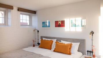 Quarto com cama, duas almofadas, mesa de cabeceira, abajur e três quadros na parede.