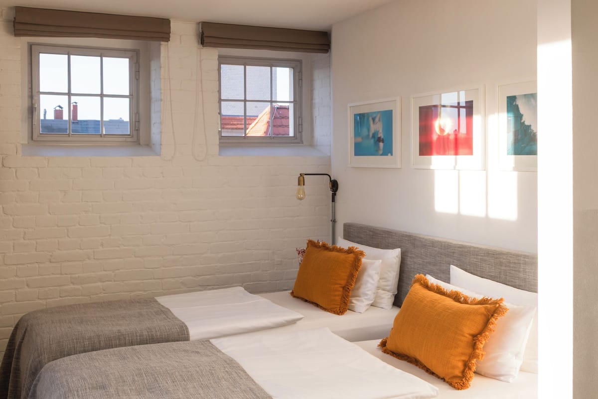 A hotel room with two beds, a brick wall, and two windows with curtains.