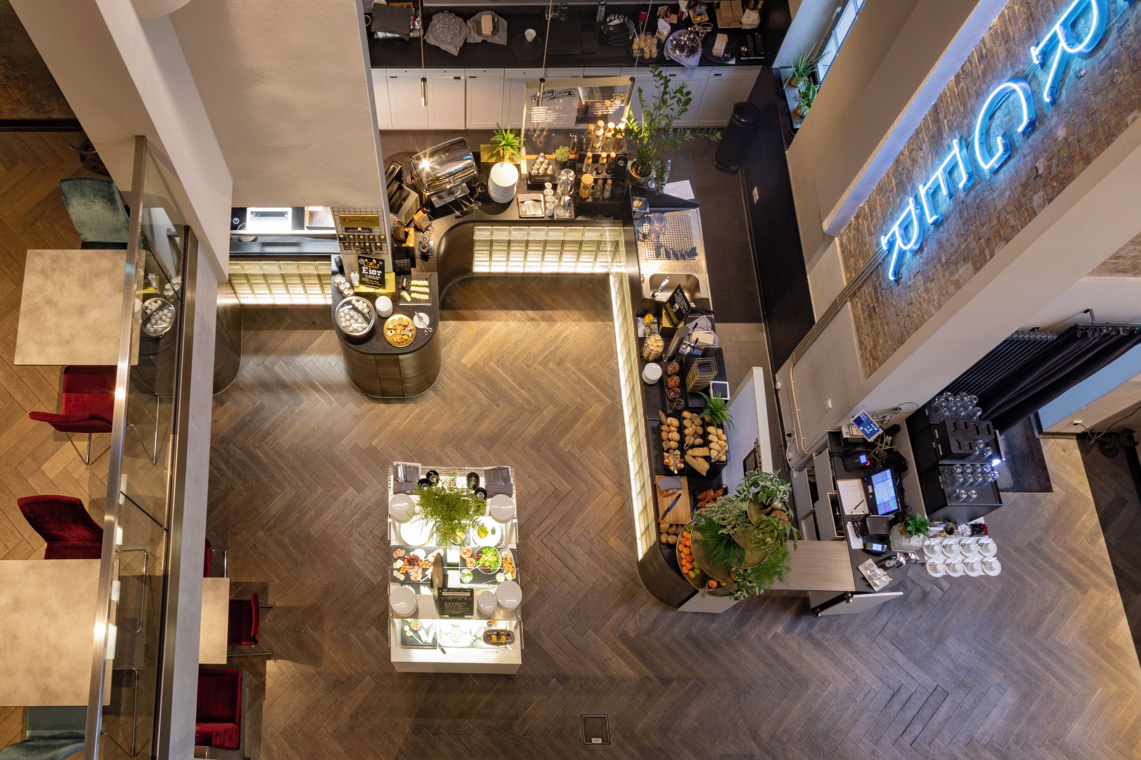 A high-ceilinged, open-plan restaurant with a central dining area, a bar, and a counter with a neon sign.