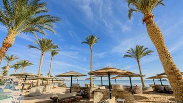 A beachside resort with palm trees, sun loungers, and umbrellas.