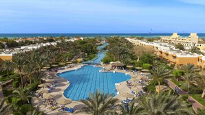 A resort with a large swimming pool, palm trees, and a view of the ocean.