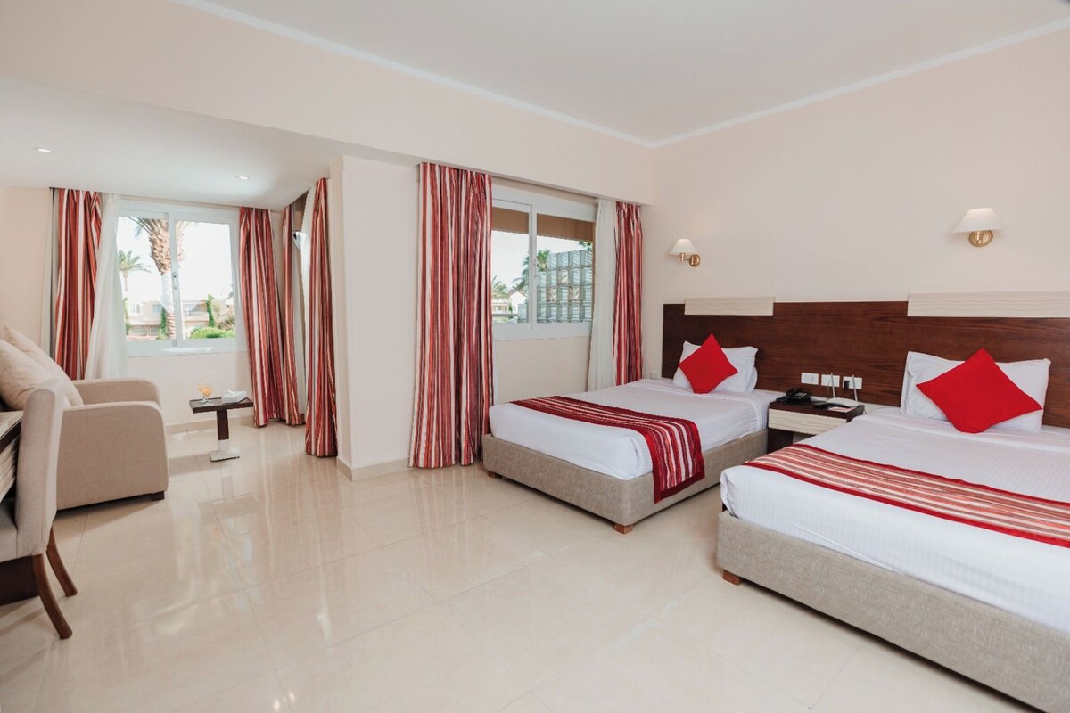 A hotel room with two beds, a sofa, a small table, and a window with curtains.