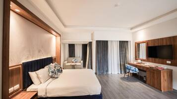 A hotel room with a large bed, a desk, a chair, a TV, and a small table.