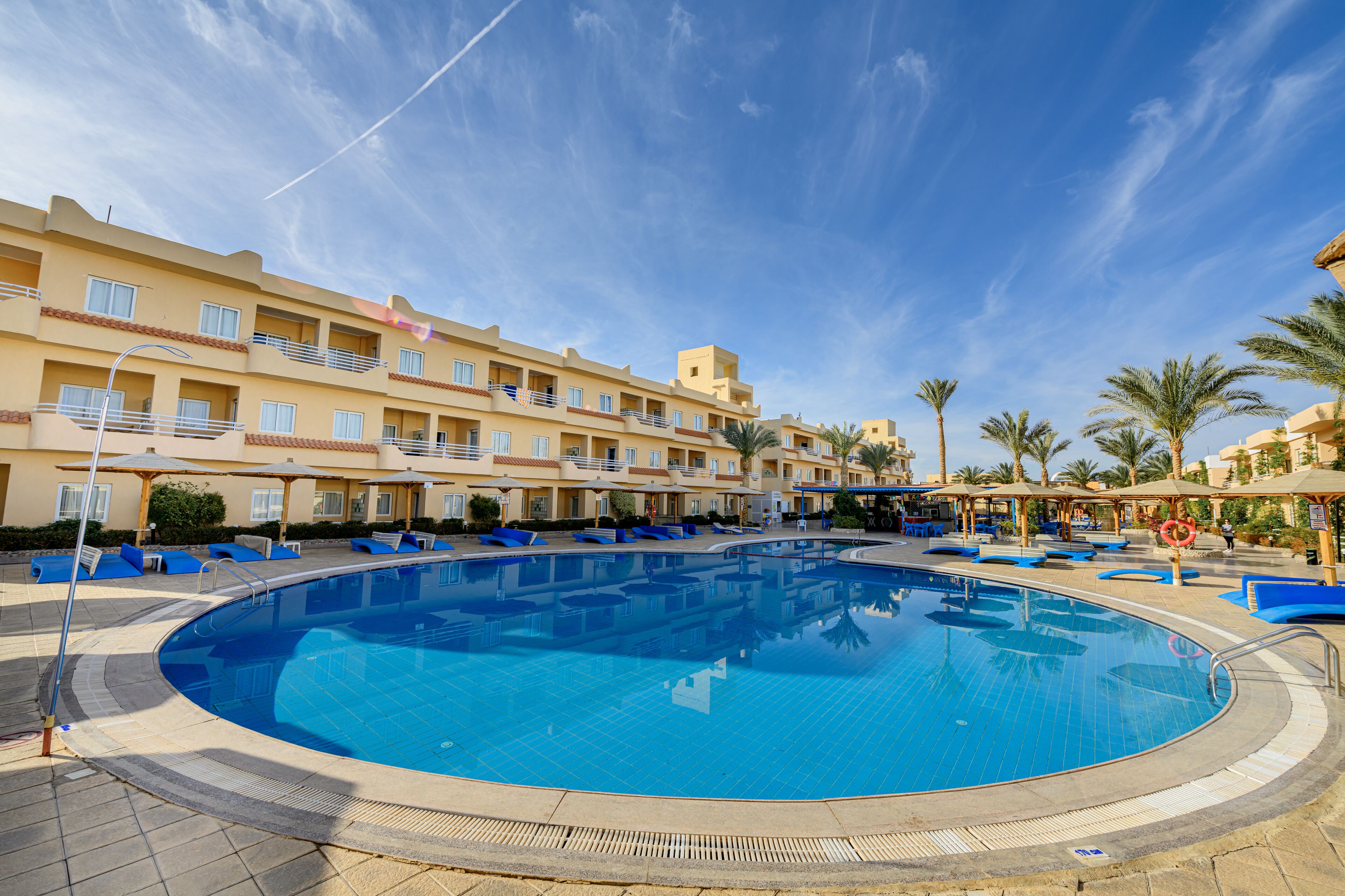 A swimming pool surrounded by lounge chairs and umbrellas, with a building in the background.