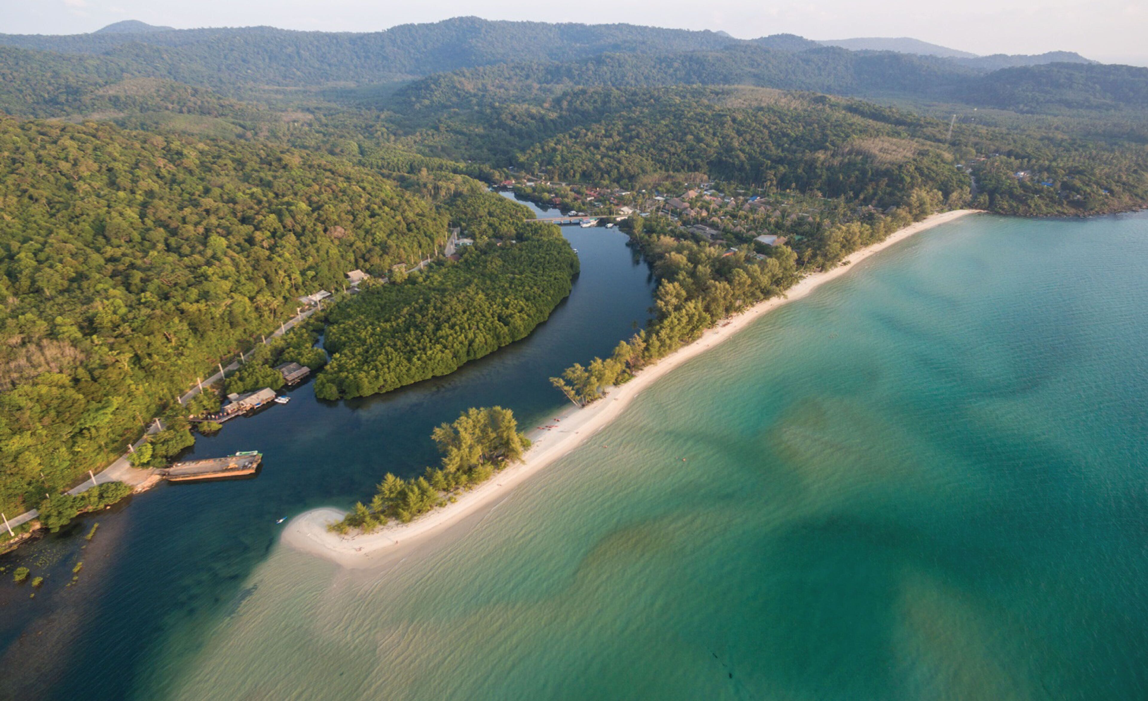 Vista aérea de una zona costera con playa, río y colinas boscosas.
