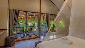 A bedroom with a bed, a window with curtains, a small table, and a chair.