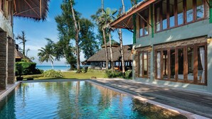 A resort with a swimming pool, beachfront views, and thatched-roof structures.