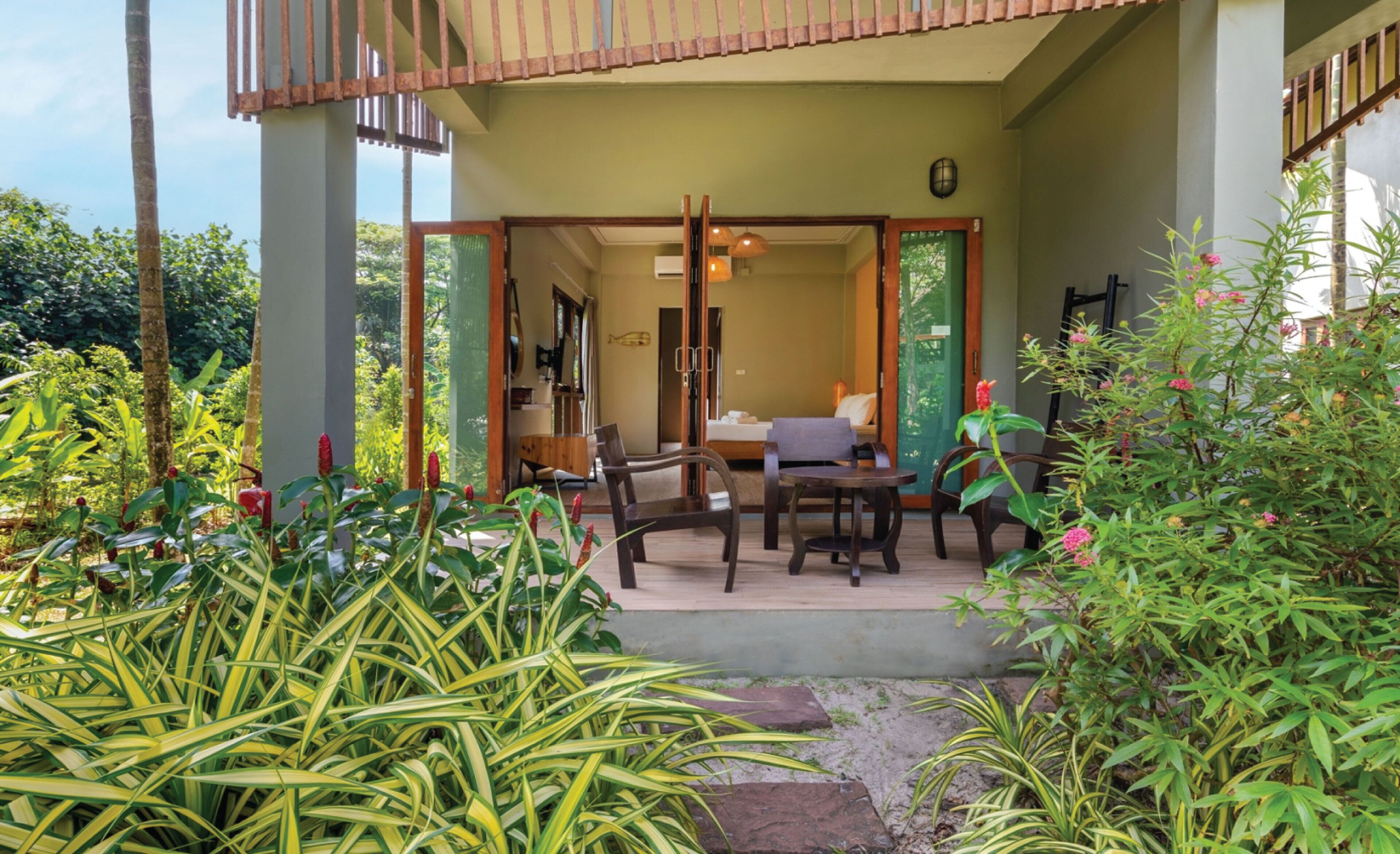 Un amplio espacio al aire libre con una terraza de madera, una zona de estar con mesa y sillas, y abundante vegetación que lo rodea.