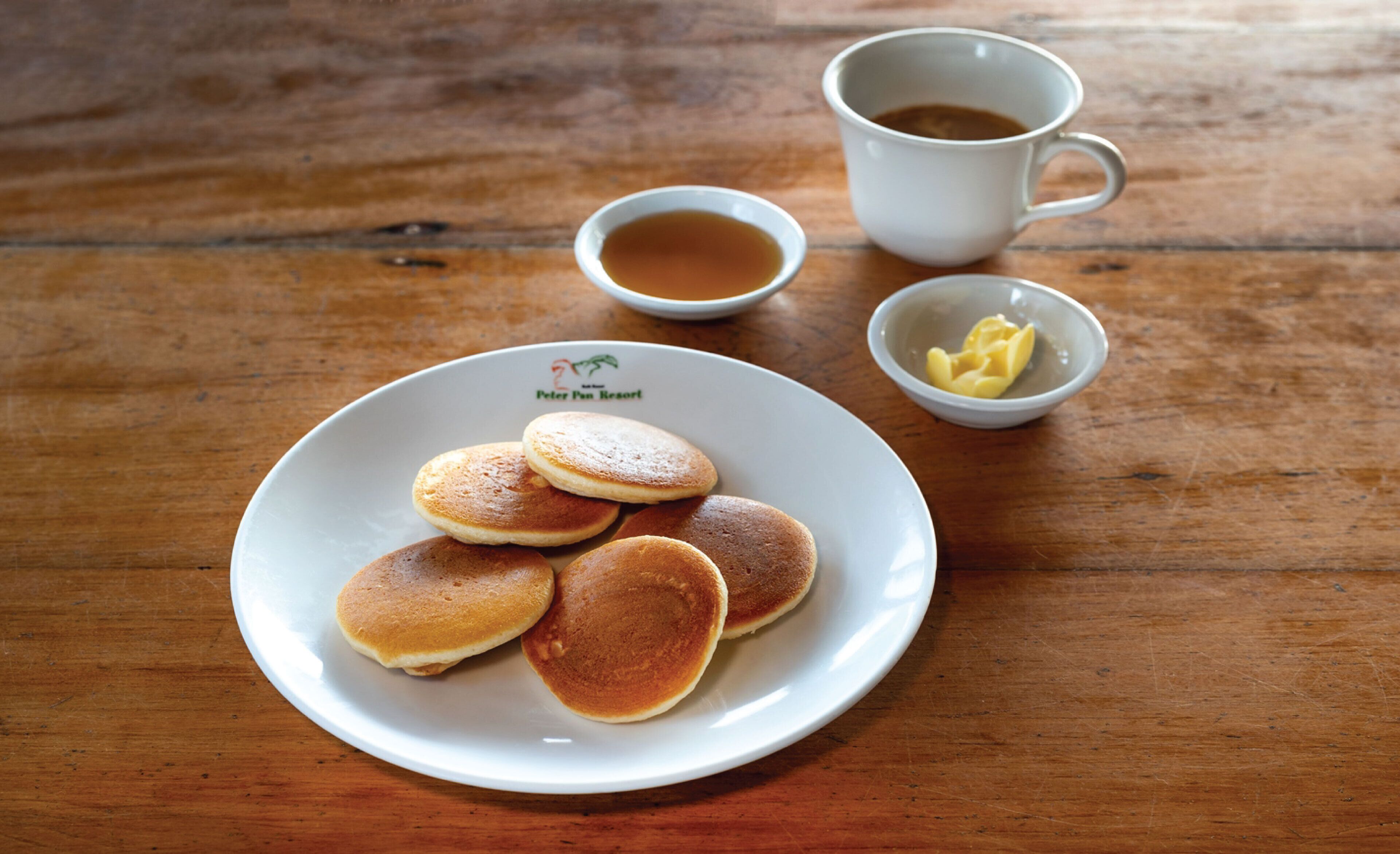 A plate of pancakes with syrup and butter on a wooden table.