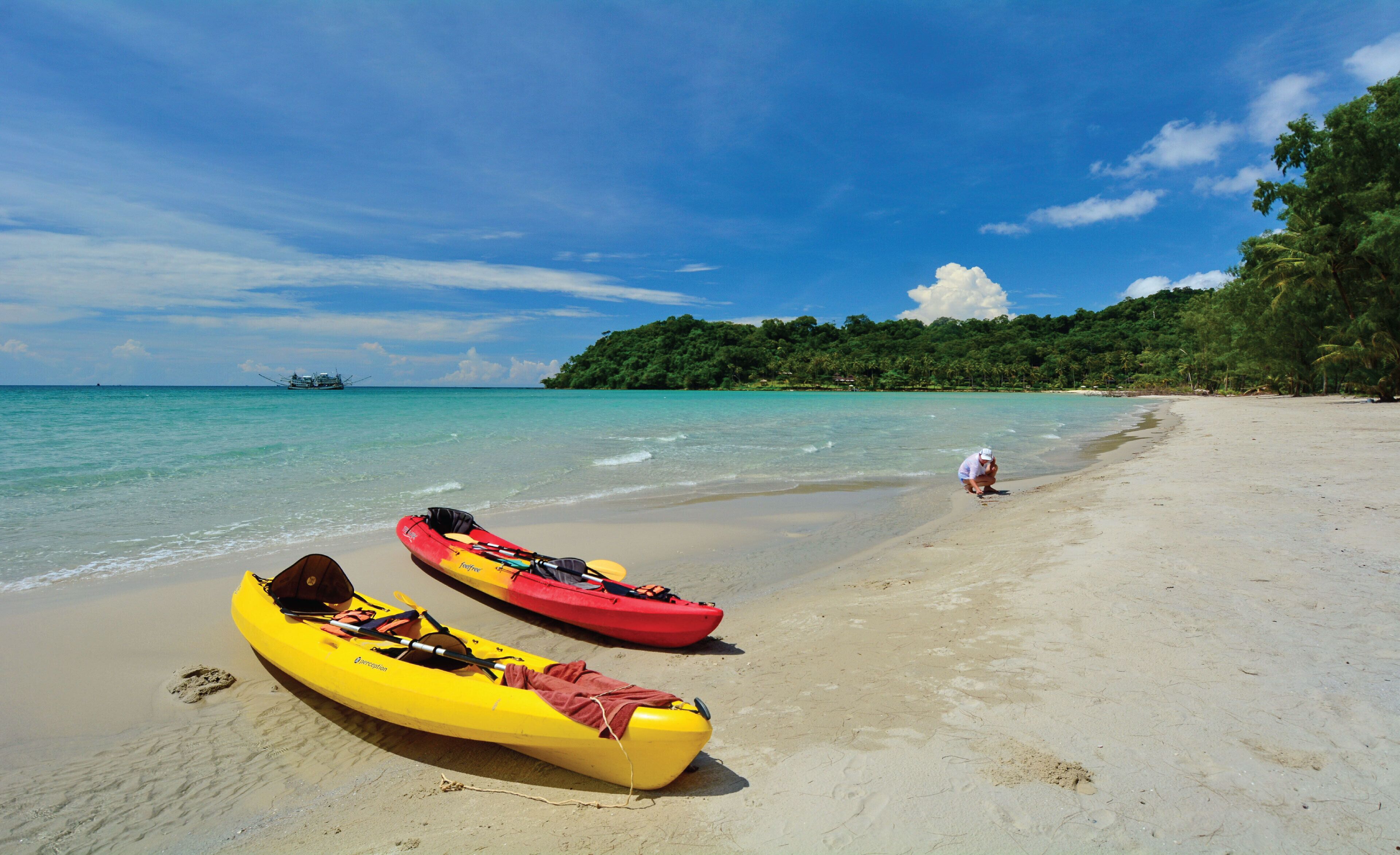 A beach with two kayaks and a person in the water.