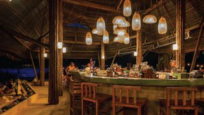 An outdoor bar area with wooden chairs and a counter stocked with bottles. - Peter Pan Resort (Ko Kood)