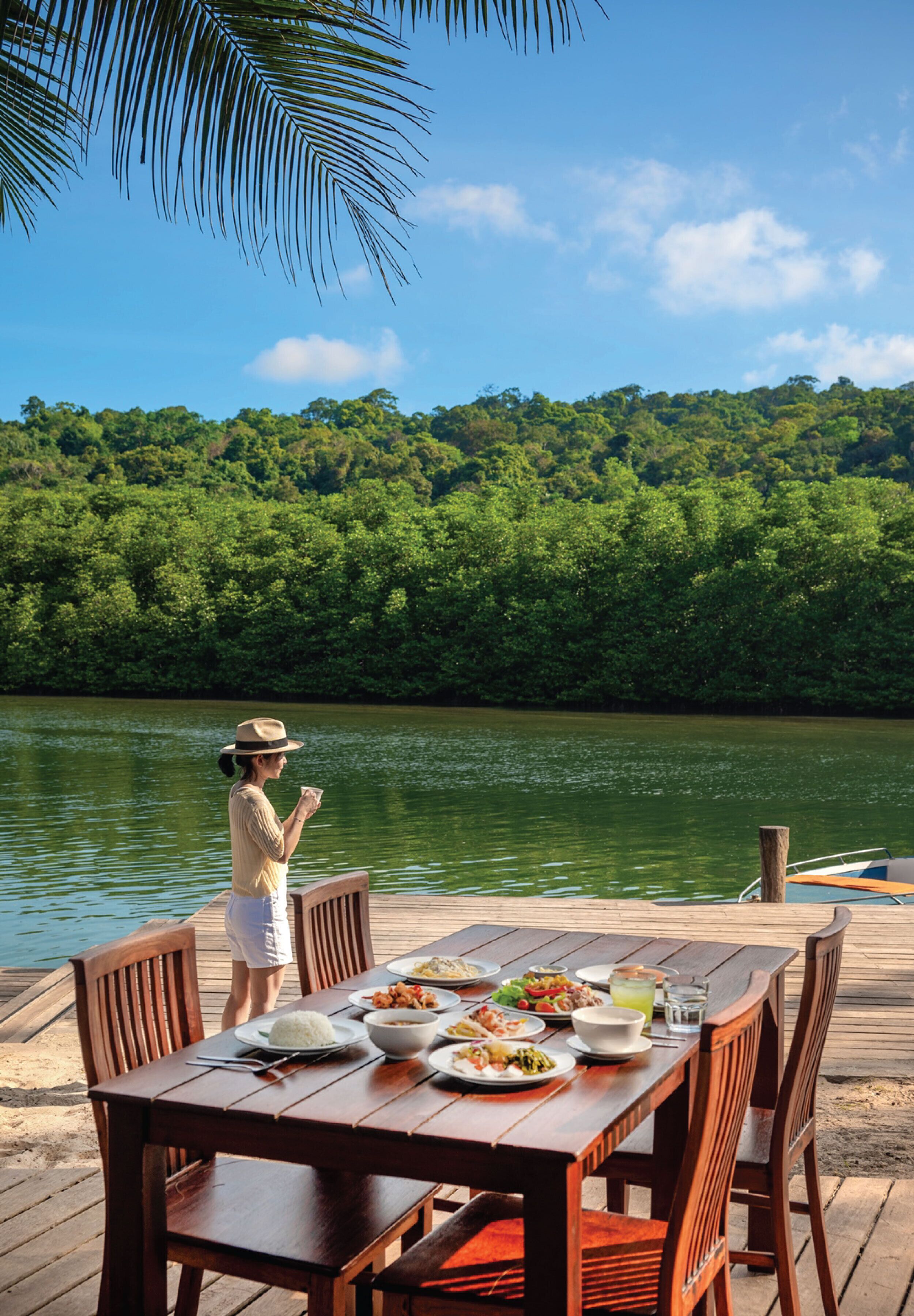 A wooden deck with a table set for a meal, overlooking a river and dense greenery.