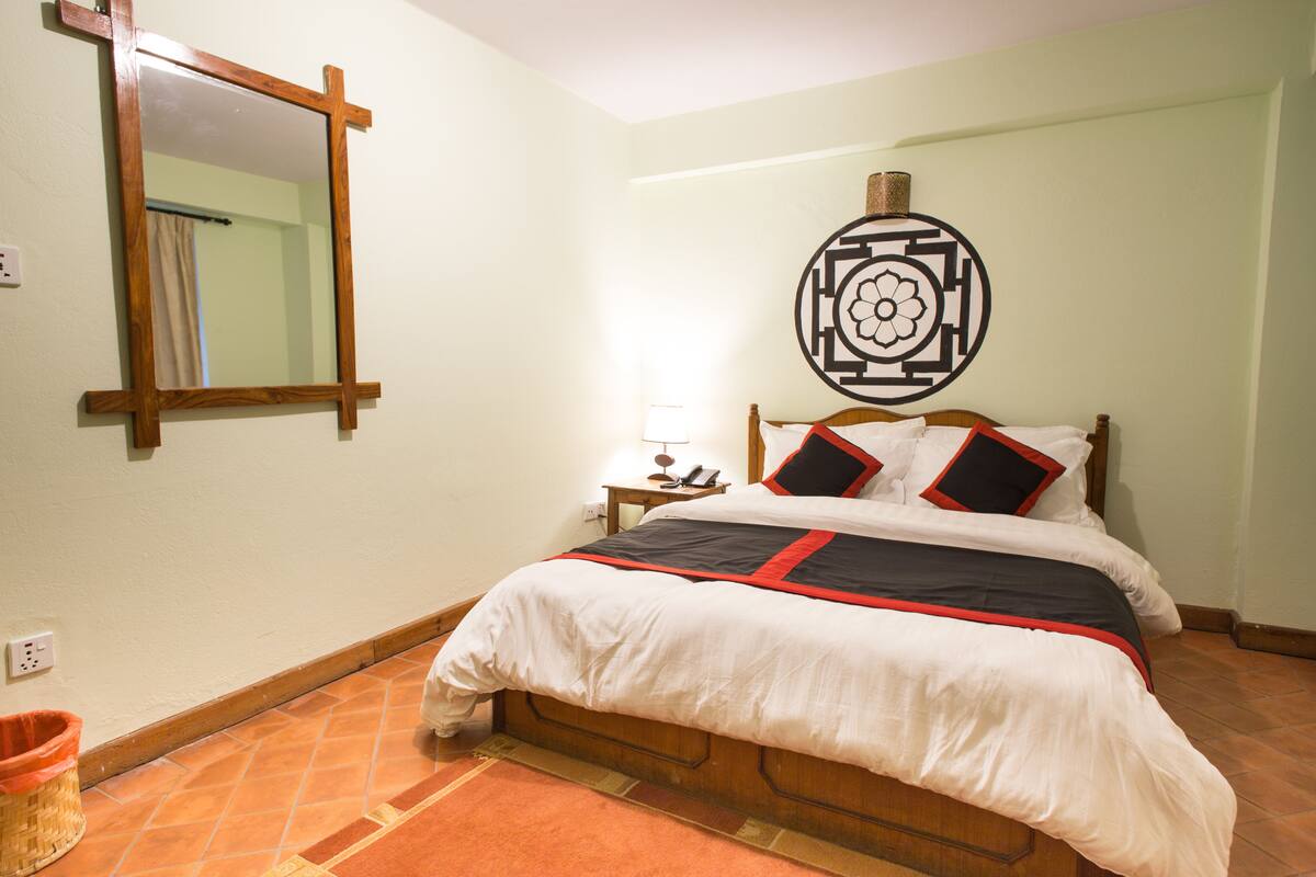 Un dormitorio con una cama de madera, una mesita de noche con una lámpara, un espejo y un adorno en la pared.