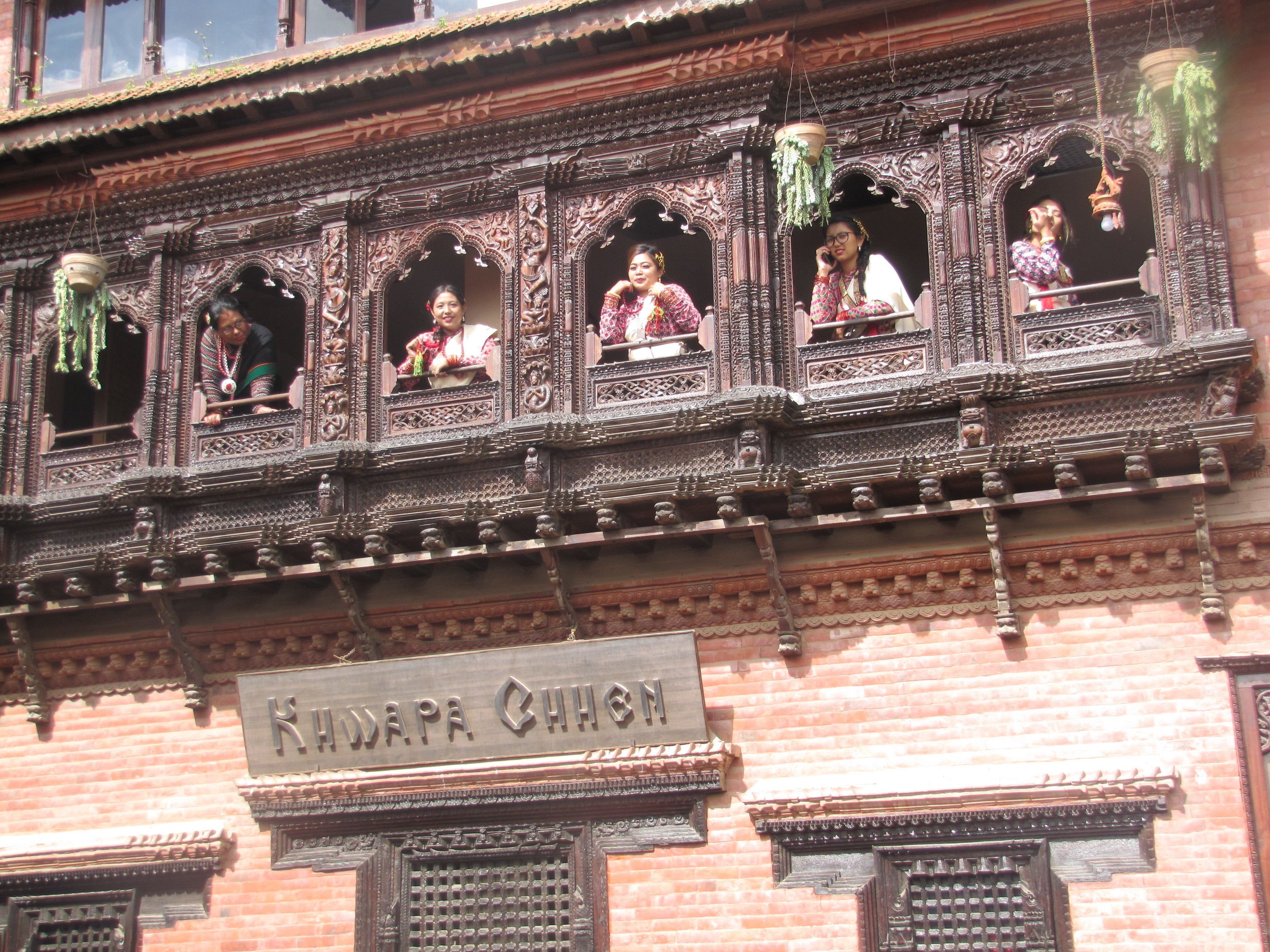 A building facade with intricate carvings and a sign reading "Khwapa Chhish".