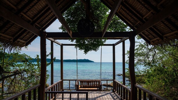Una terraza de madera con un banco, con vista a un cuerpo de agua y una isla distante.