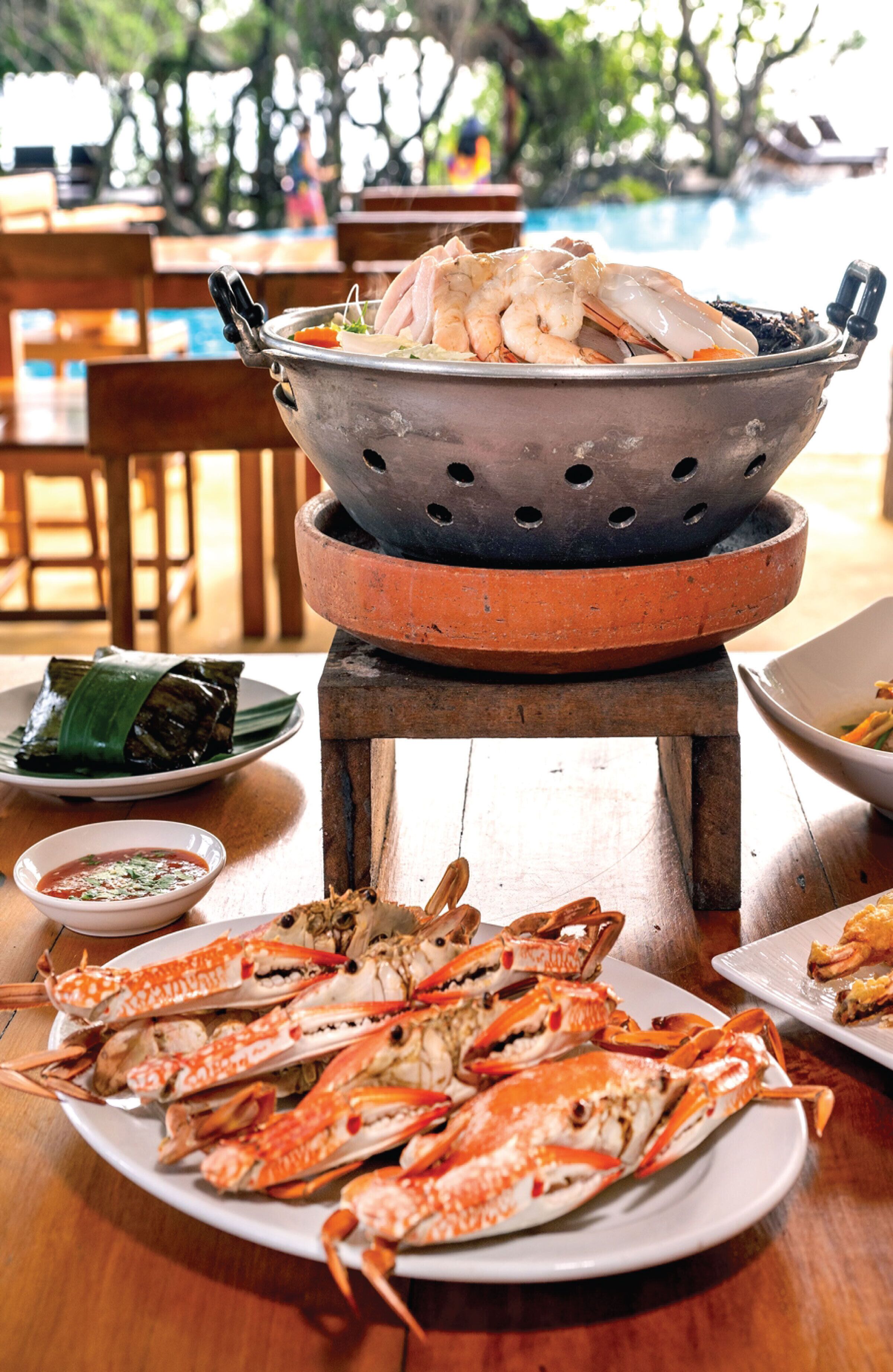 A seafood dish with a steaming pot and plates of crabs and shrimp.