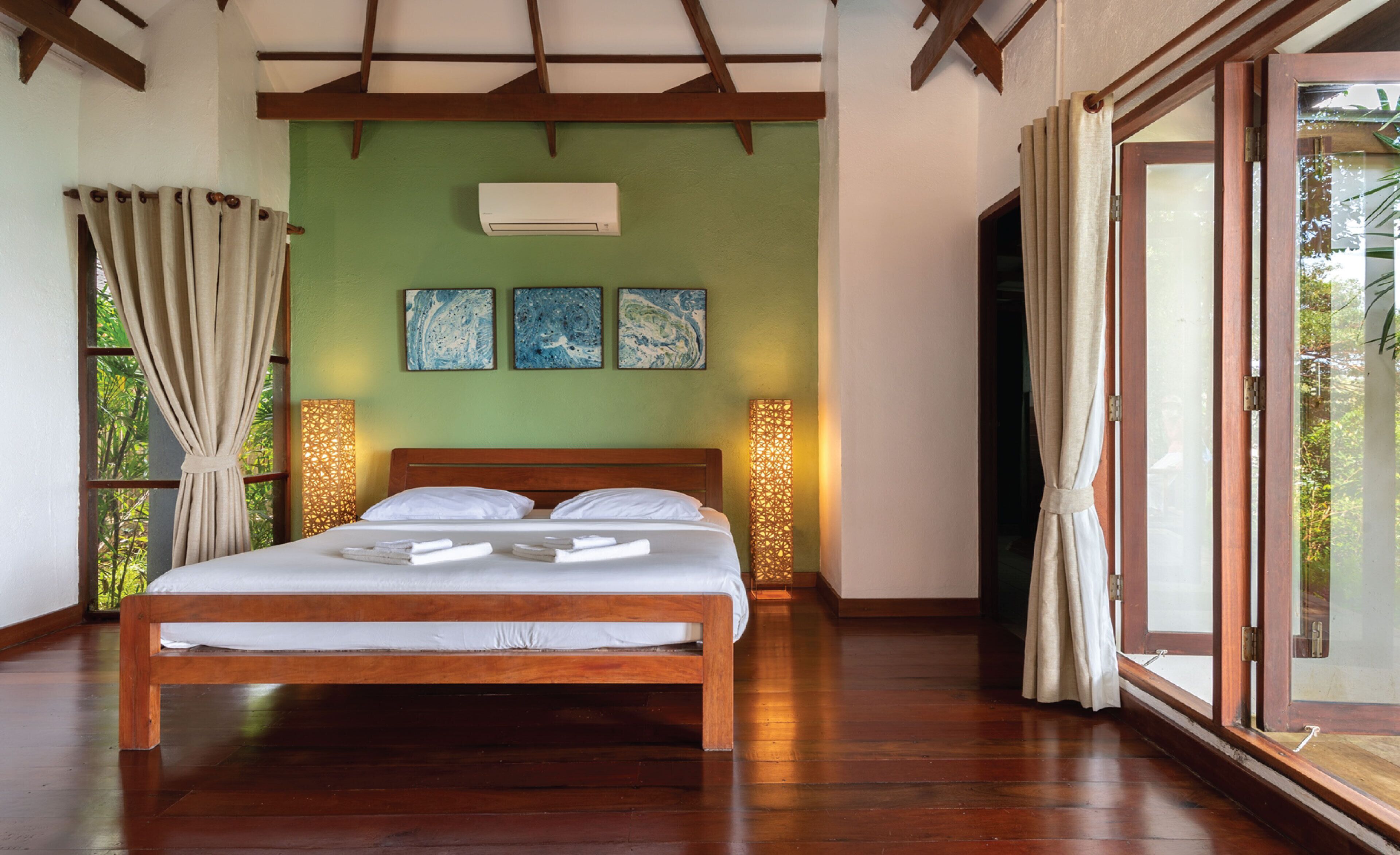 A spacious bedroom with a wooden bed, green walls, and a large window with curtains.