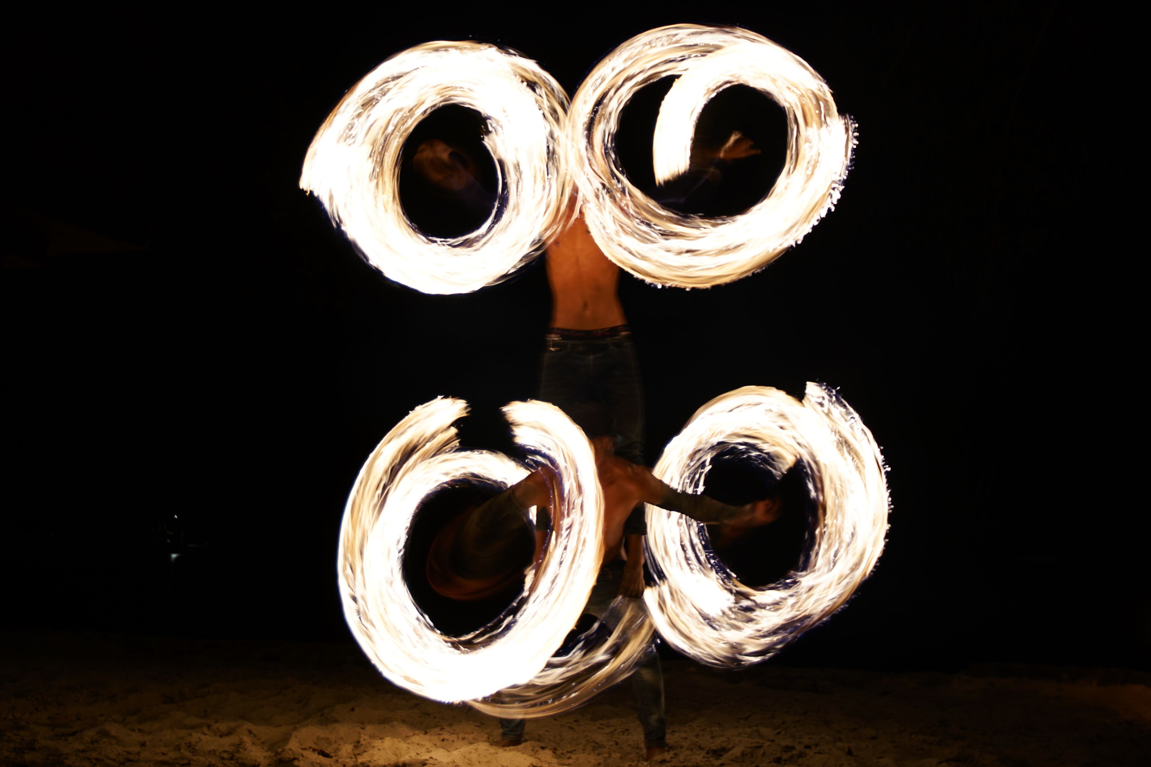 Una persona haciendo malabares con fuego usando cuatro aros llameantes.