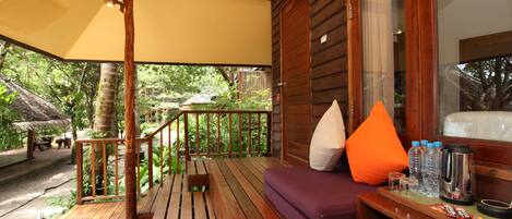 A wooden deck with a sofa and cushions, a coffee table with snacks and a kettle, and a magazine on the floor.