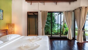 Habitación de hotel con cama, cabecera de madera, mesita de noche, lámpara y vista a zonas verdes por la ventana.