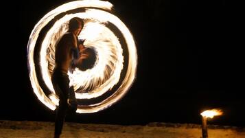 Una persona realizando una exhibición de malabares con fuego en un entorno exterior oscuro.