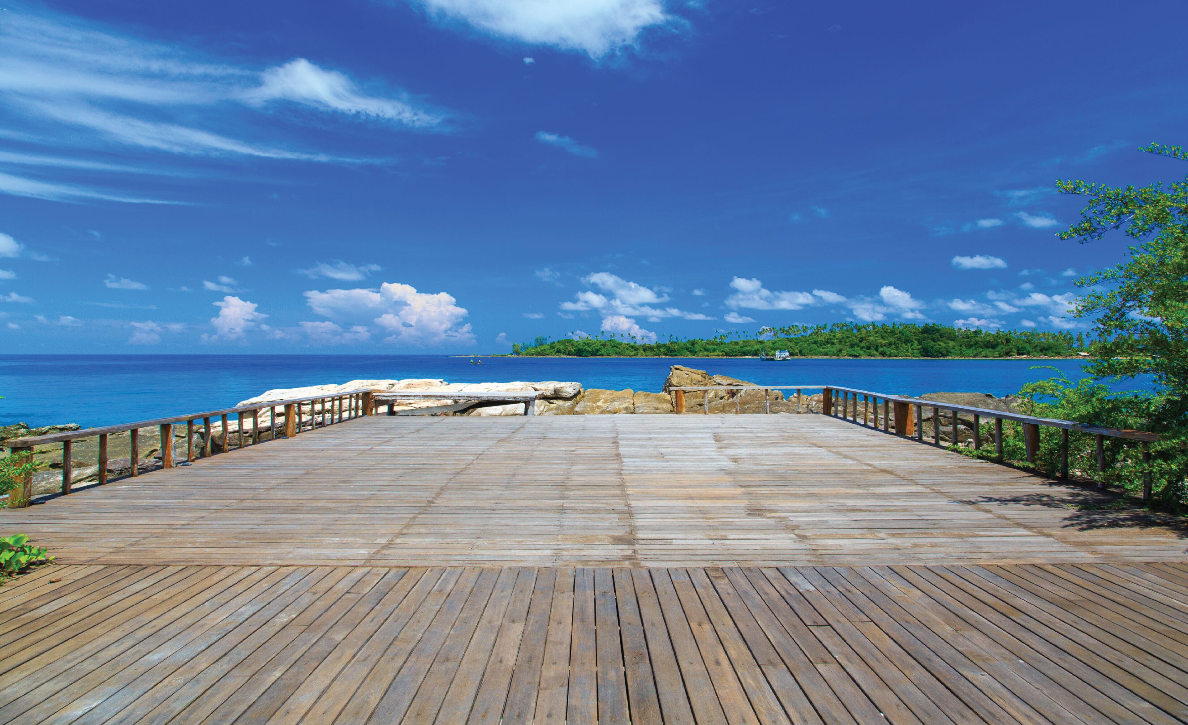 Un muelle de madera que conduce a una playa con aguas azules cristalinas y una isla distante.