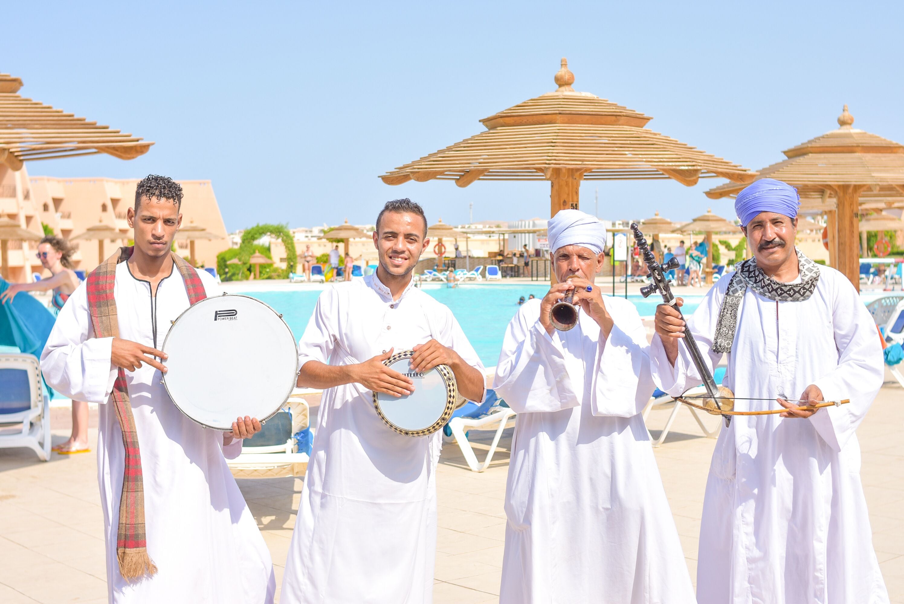 A group of people in traditional attire by a poolside with umbrellas and lounge chairs.