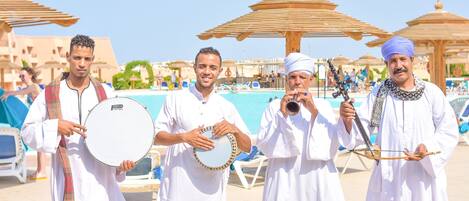 A group of people in traditional attire by a poolside with umbrellas and lounge chairs.