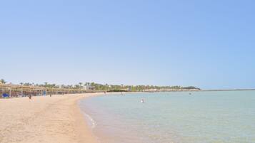 A beach with clear water, a sandy shore, and a row of beach umbrellas.
